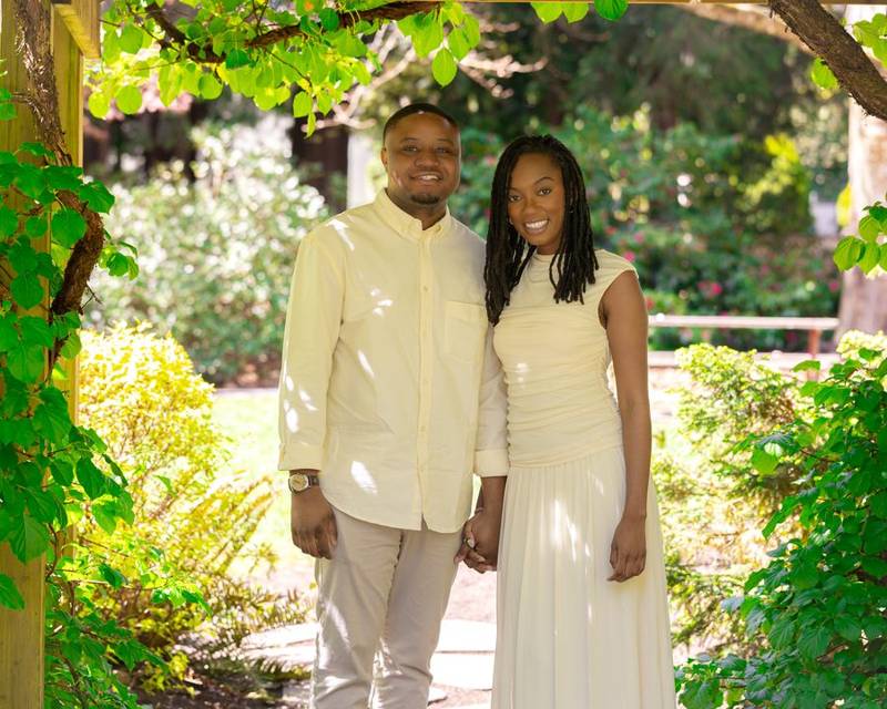 Engaged couple in cream outfits under a garden pergola