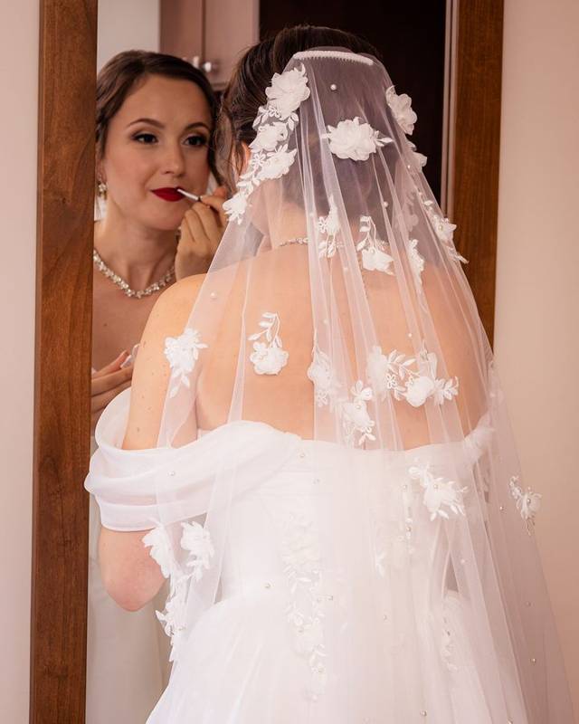 Bride putting on lipstick in the mirror, wearing a floral veil