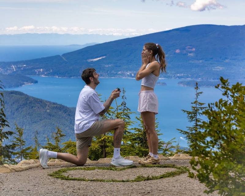 Surprise proposal at Bowen Lookout on Cypress Mountain: he kneels with the ring as she covers her face in surprise, Howe Sound behind them