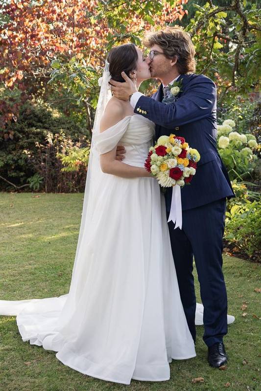 Couple kissing in front of autumn leaves, bride holding a red and yellow bouquet