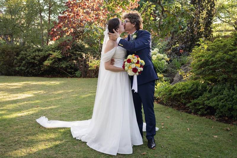 Bride and groom kissing on a lawn under autumn trees, her long train spread on the grass