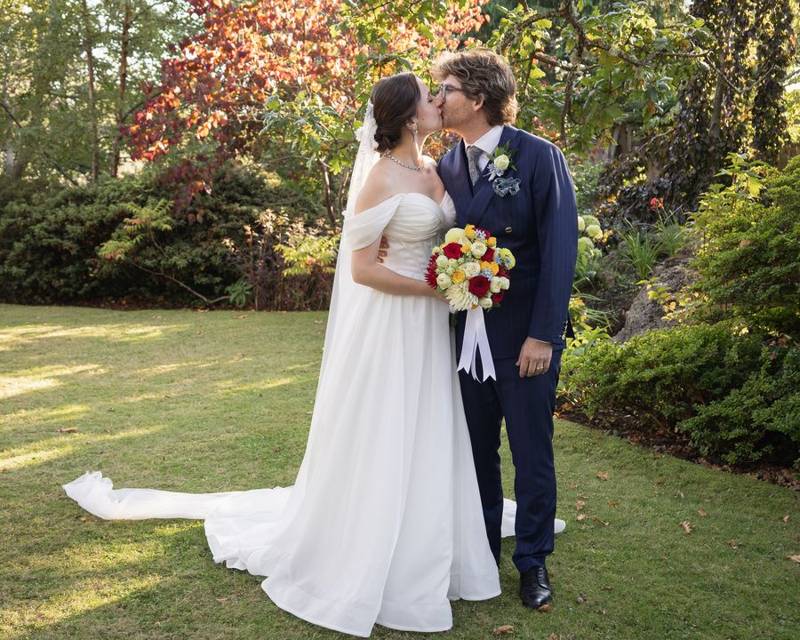 Newlyweds kissing on a lawn framed by autumn trees